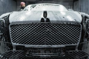 A close-up of a luxurious black car being cleaned with foamy soap at a carwash.