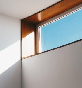 A minimalist interior showcasing sunlight streaming through a modern glass window against a blue sky.